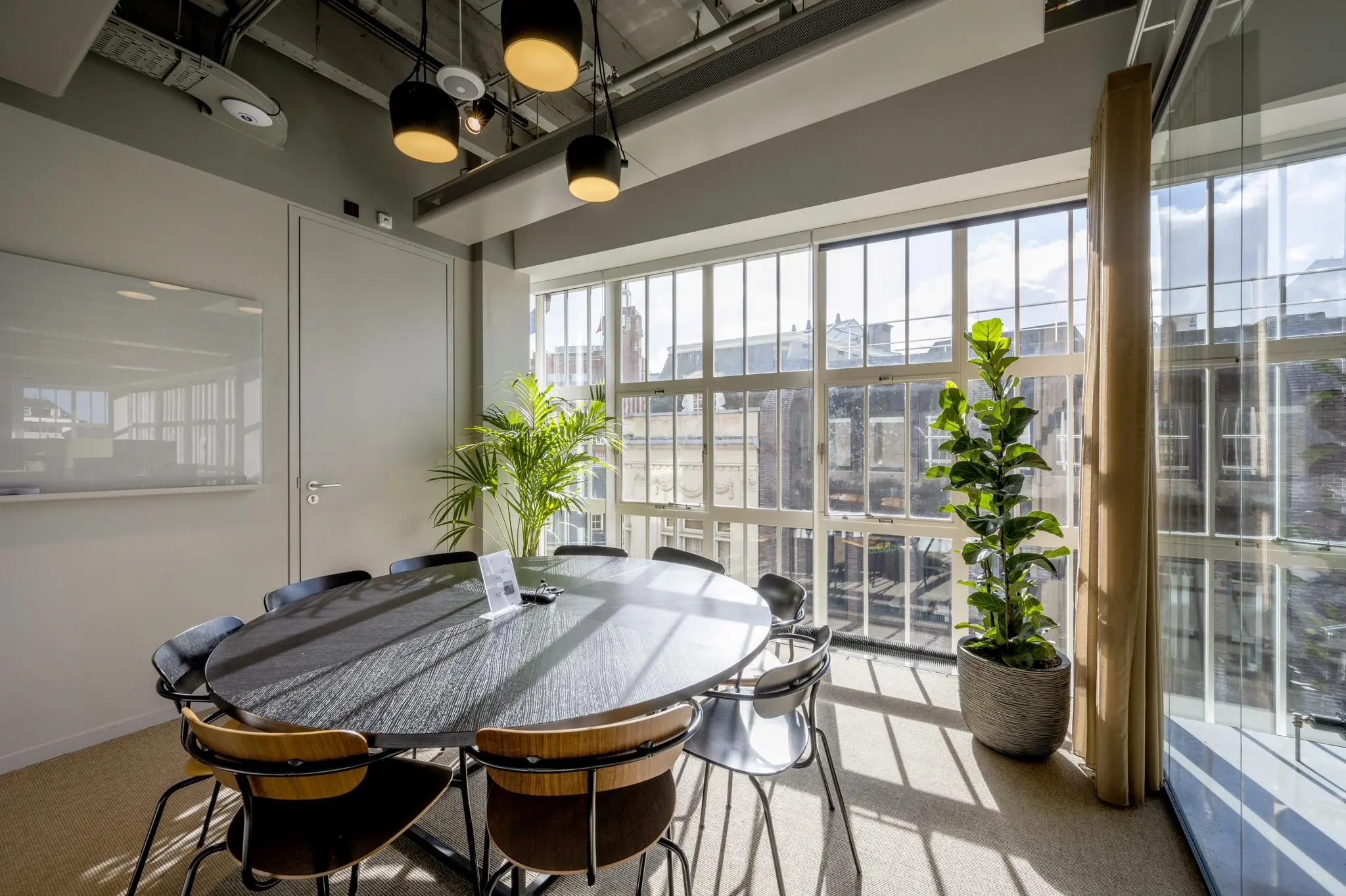 Vergaderruimte met ronde tafel, zes stoelen, grote ramen en uitzicht op de Sint Jorissteeg.